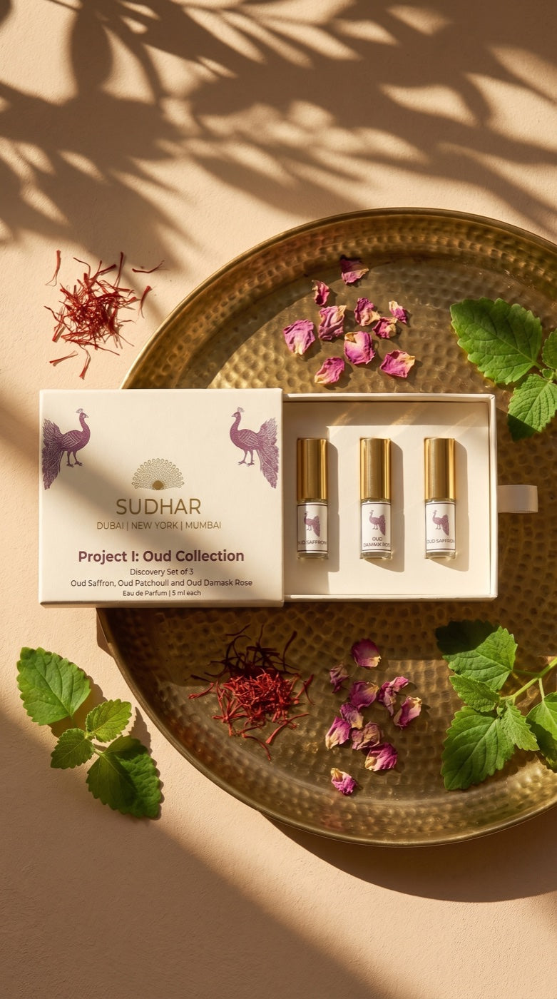 The Discovery Set of 3 — open box with three oud eau de parfum on a brass tray, saffron, rose petals and mint in golden light